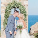 The couples first kiss at the end of their celebrant led wedding ceremony at Villa Delenia in Evia Greece. The couple are wearing Greek wedding crowns.