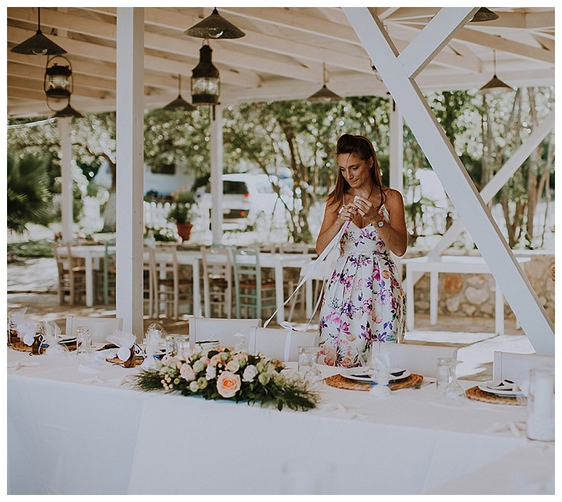 A young woman in a flowery dress is arranging flowers on a table in a greek beachside restaurant, getting ready for a wedding in lefkas