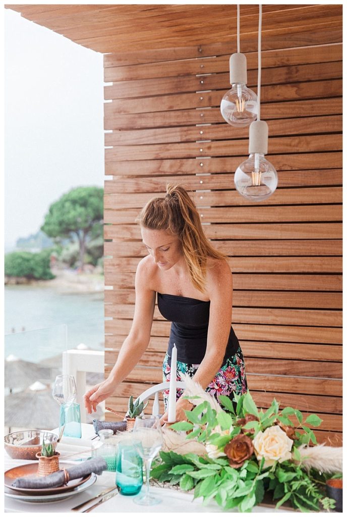 Under a wooden shelter with a pool in the background, Claire from lefkas weddings adjust a floral display getting ready for a wedding ceremony in Lefkas