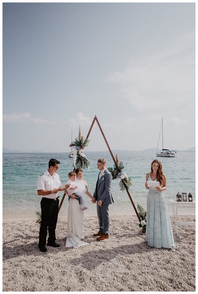 A newly wedded coupe with the registrar and claire from Lefkas weddings on a beach in Lefkas. The photo is of their wedding ceremony in lefkas