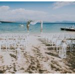 A setting for a beach wedding in Lefkas with chairs and a wedding arch on the beach with the sea in the background.