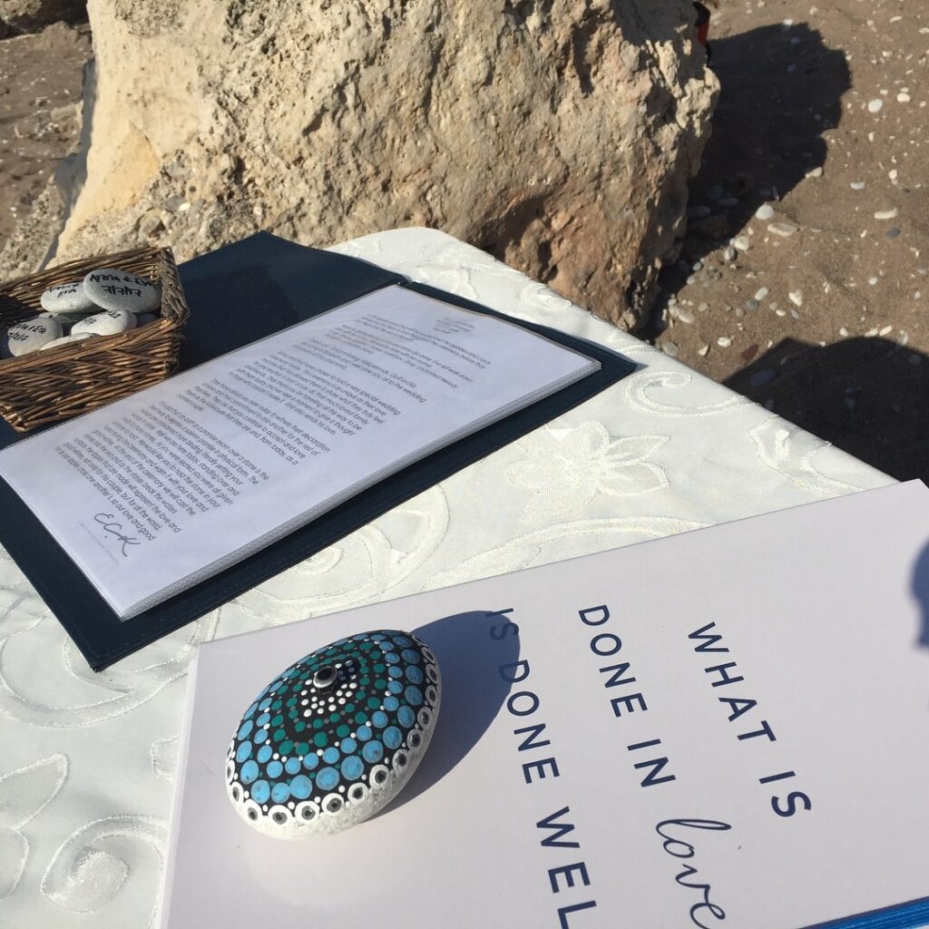 A folder with a wedding ceremony script and a stone painted with a mandala and a greek eye in the centre, used for an oath stone in a gay wedding ceremony on a beach in Rhodes